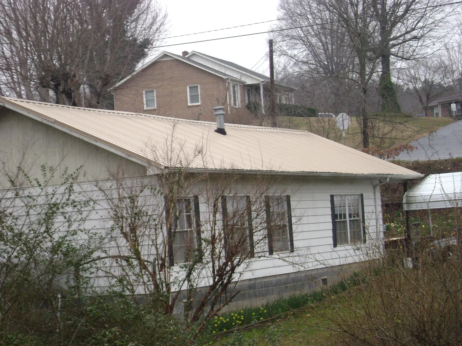 Tan metal roof on a white sided house set into a hillside — Commercial Roofing by Roofing Brothers in Palm City
